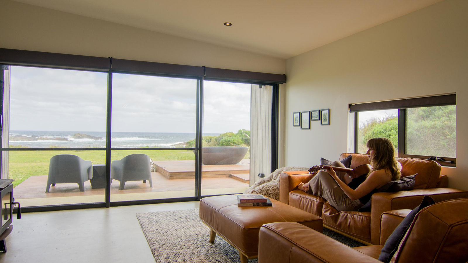 Guest relaxing on a tan leather sofa with ocean views through the glass