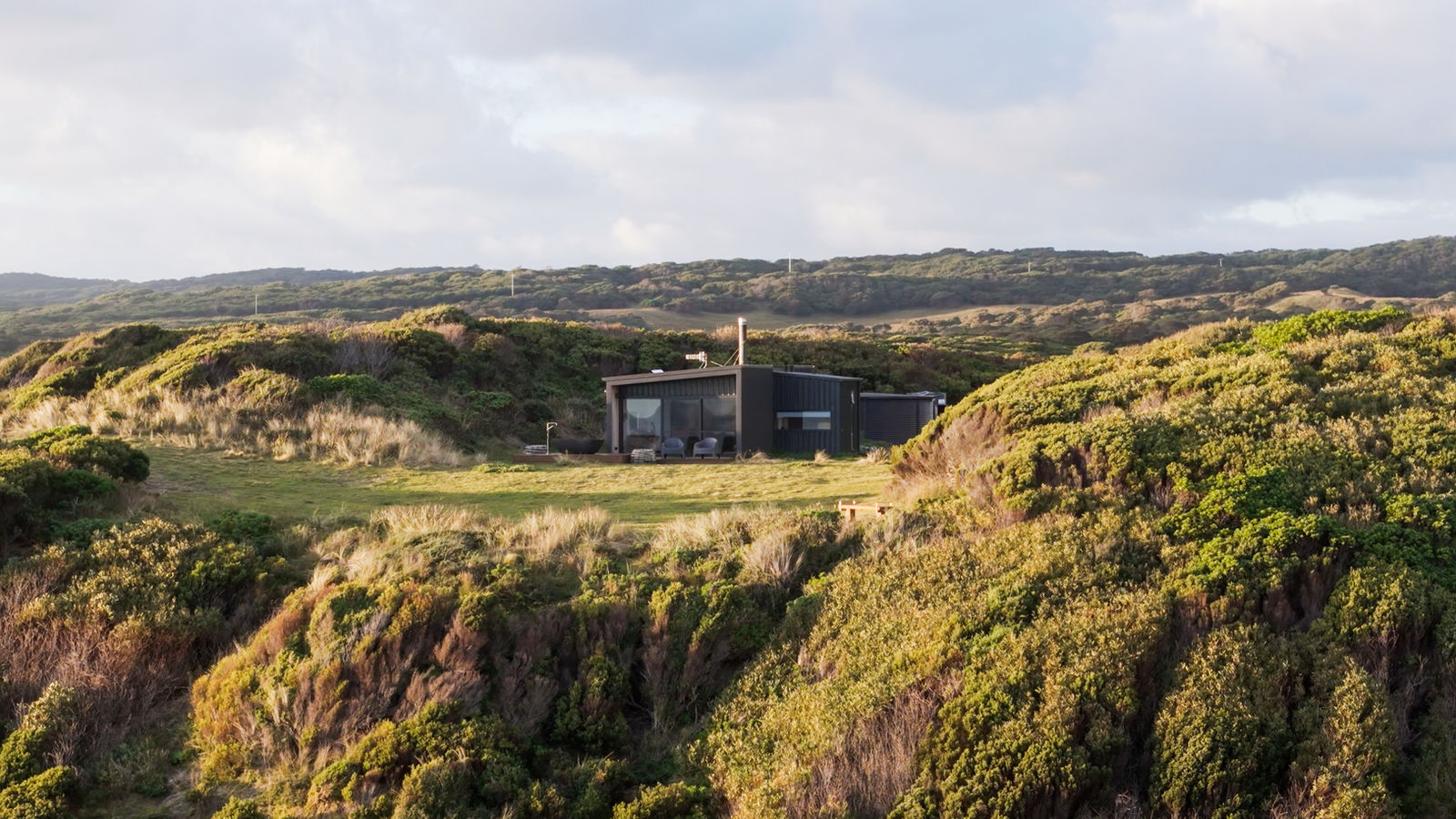 The house nestled into the coastal dunes at golden hour